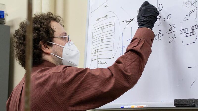 Mikhail Kats draws a figure with an equation on a white board